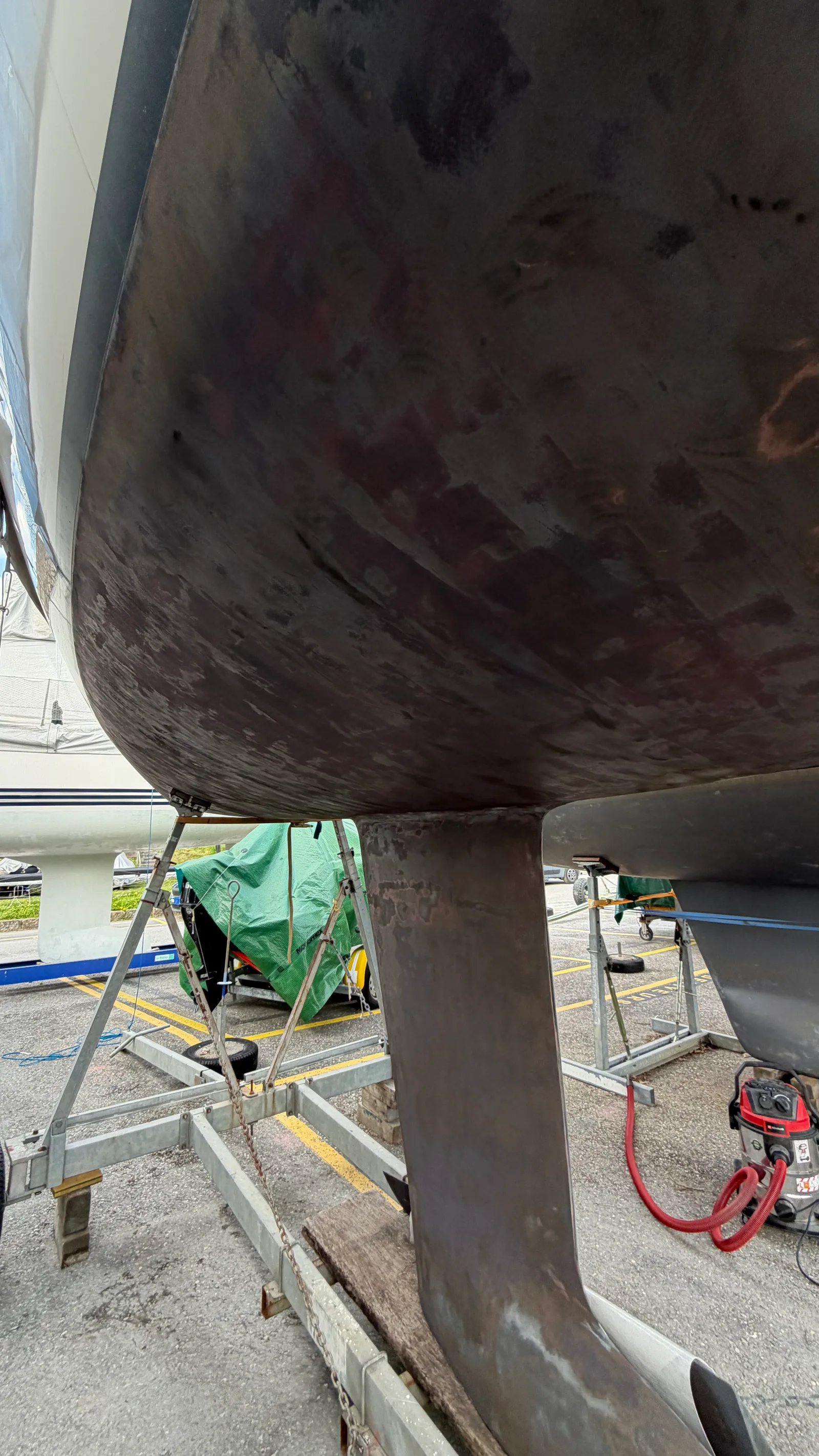 Ponçage de la coque d'un J/92s au sec : la vieille couche d'antifouling craquelée traversée à l'orbitale pour retrouver une base saine