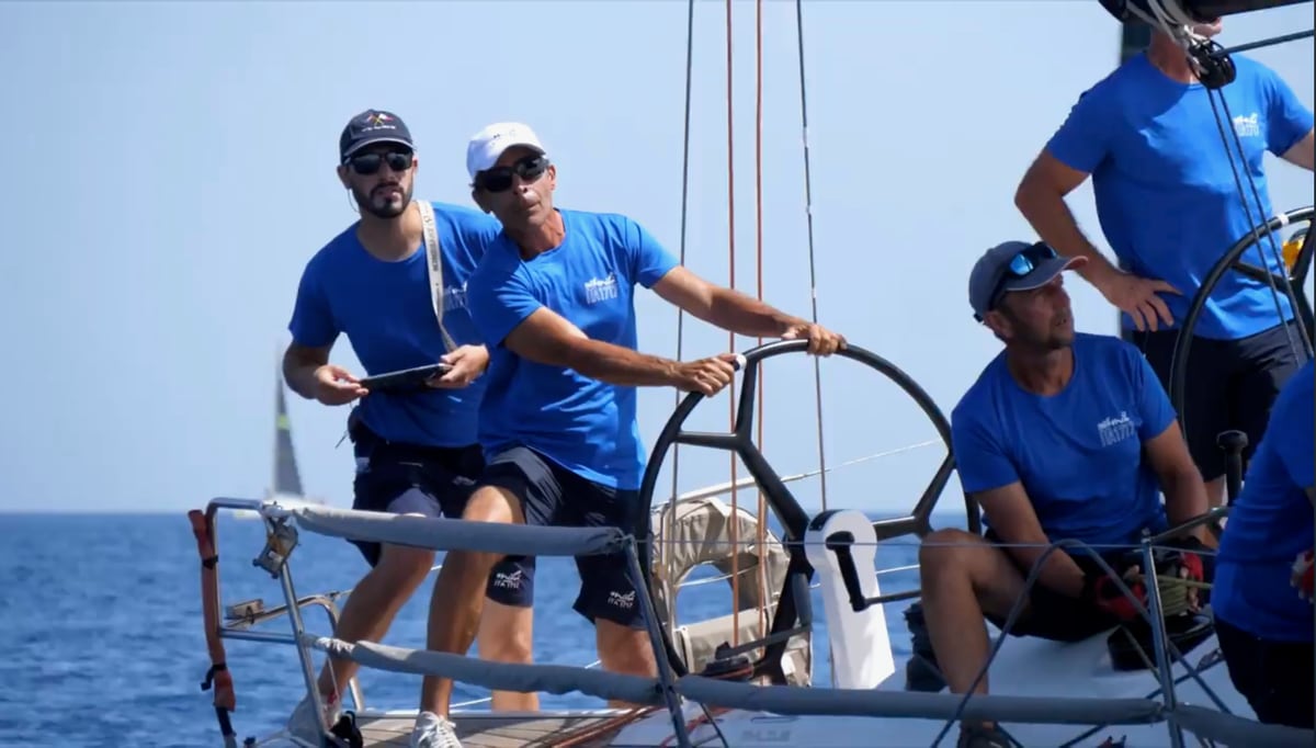 Enrico Bruschini in a blue cap, navigator, calling a tactical decision into the helmsman’s ear during a race in the Mediterranean.