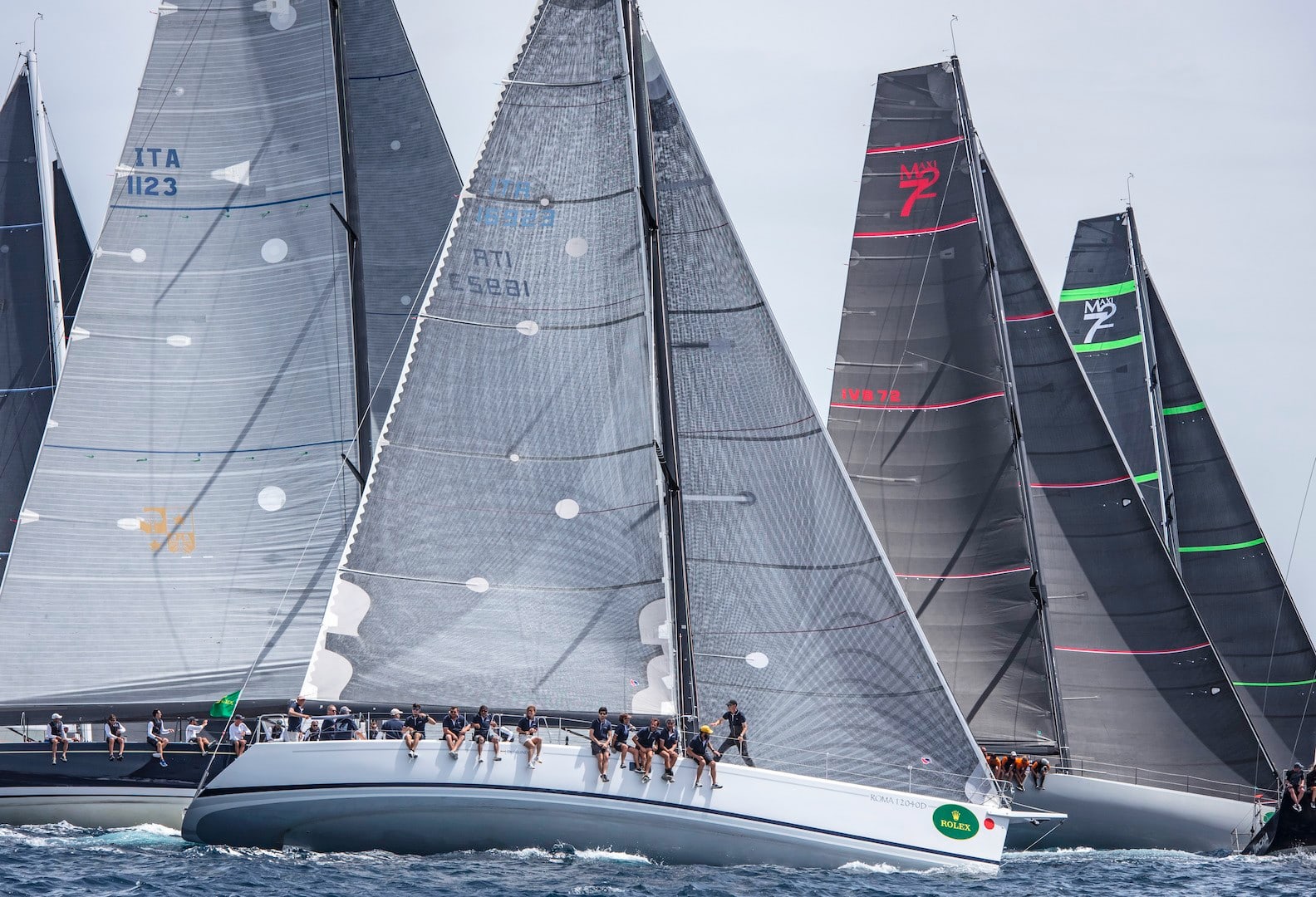 Maxi yacht fleet hard on the wind in the Mediterranean during a Rolex Giraglia race — Farr 60 and Maxi 72 sailboats, sail numbers ITA 1123, ITA 16923, ITA 12, MAXI 72 visible.