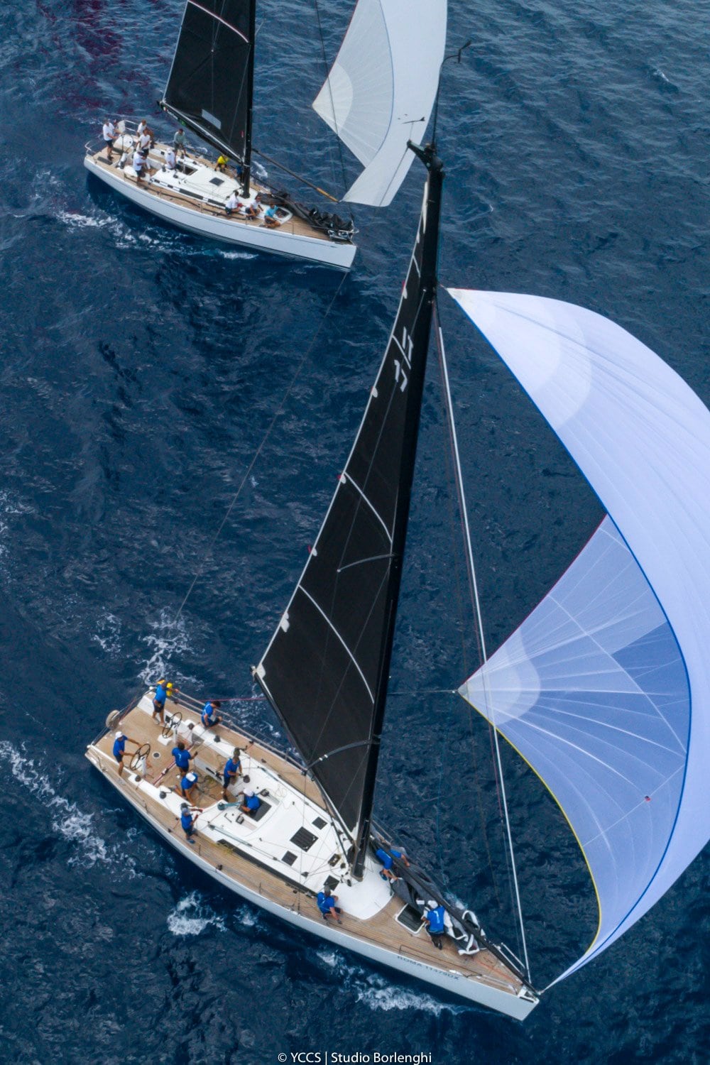 Maxi yachts racing offshore under spinnaker — aerial view of racing sailboats in the Mediterranean.